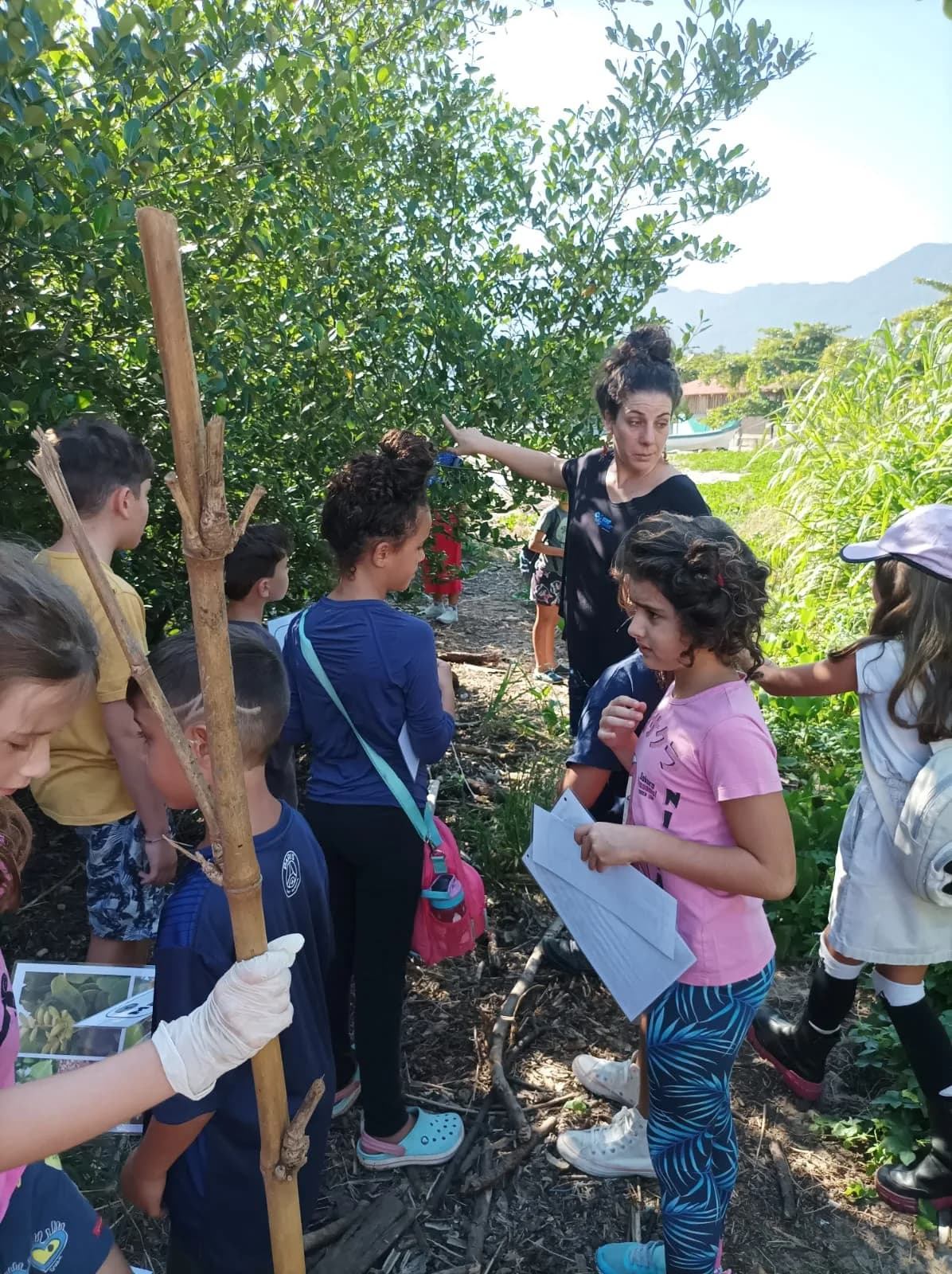 Professora e alunos em excursão ecológica com o canal de Ilhabela ao fundo
